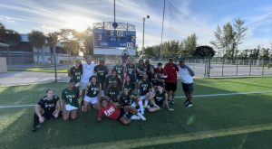 FNU women's soccer takes group picture in front of 3-2 scoreboard after beating Florida College.