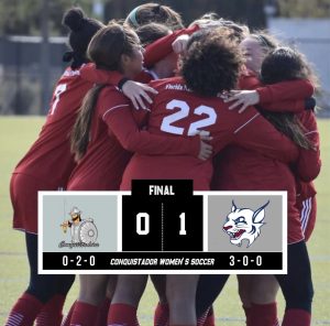 Women's soccer players huddled in a group celebrating a goal.